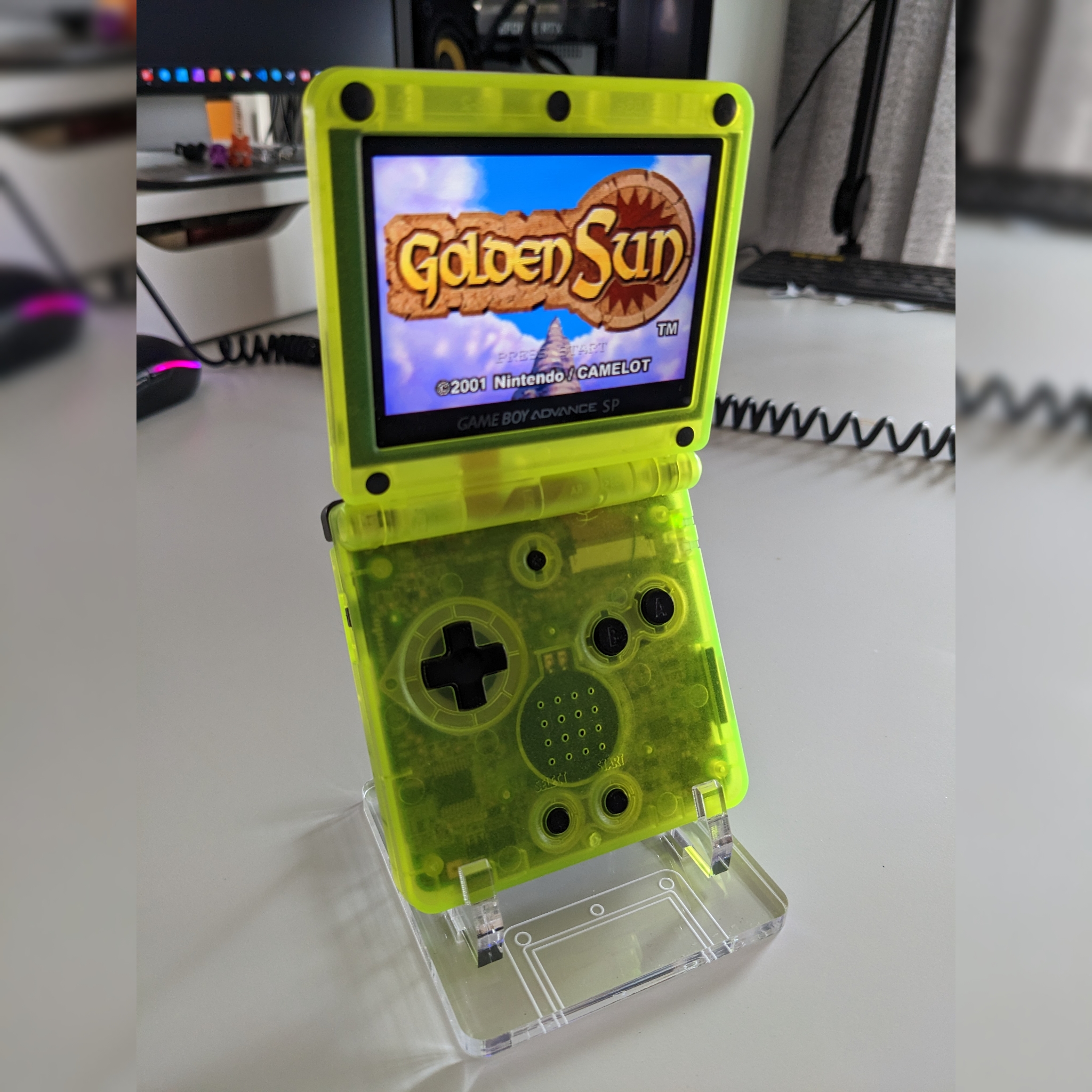 A modded GBA SP on a stand. Its case is translucent green. It is playing Golden Sun.